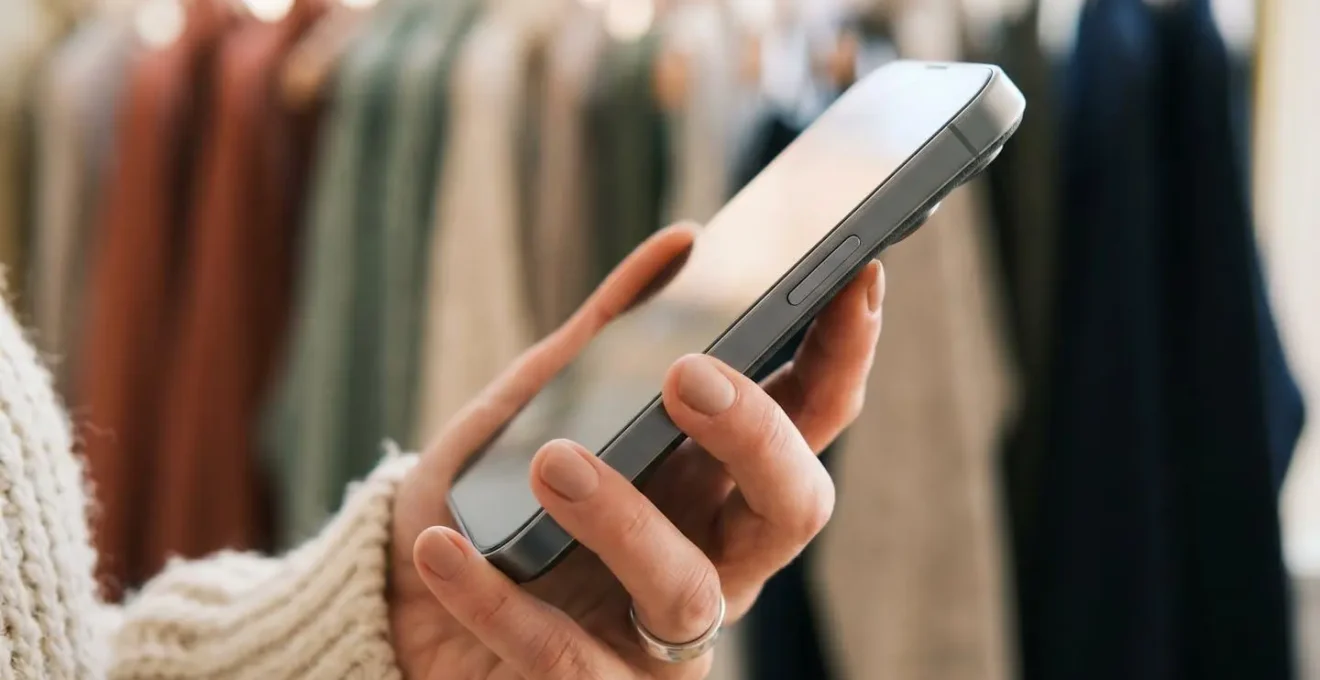 A person holding a smartphone, implying the use of a digital app to track their wardrobe inventory.